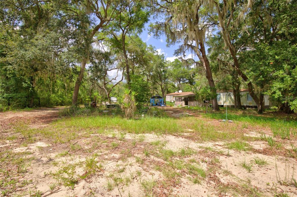 A mobile home sits on a sandy, tree-filled lot with a small blue canopy structure — 9955 SE 160TH AVENUE, OCKLAWAHA, FL
