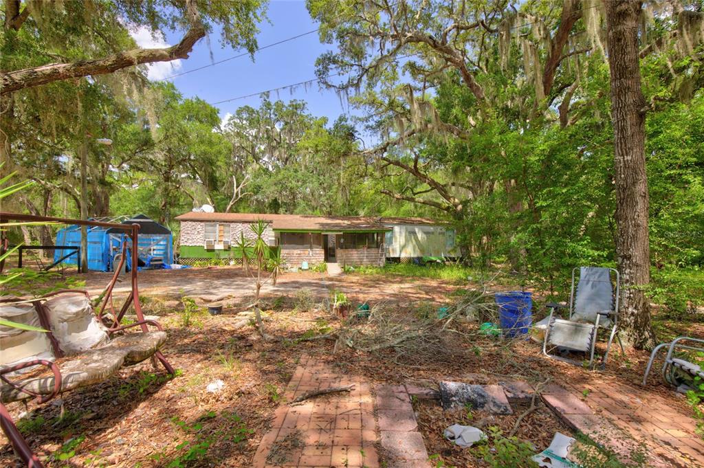 A single-story mobile home sits in a wooded lot with a brick patio in front — 9955 SE 160TH AVENUE, OCKLAWAHA, FL