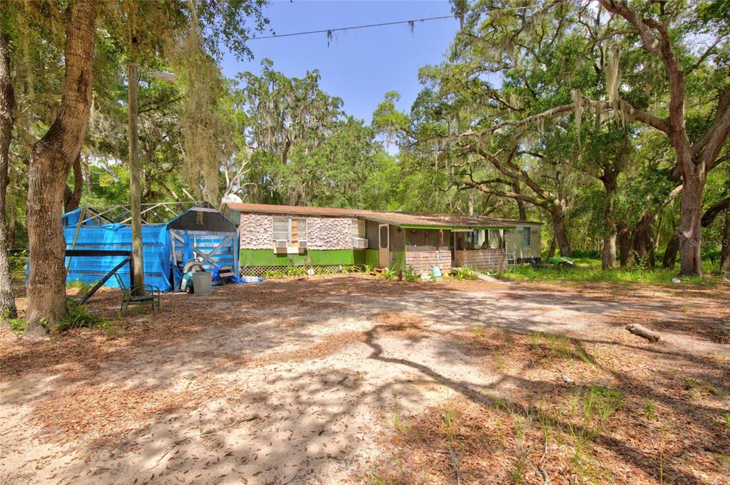 A single-story mobile home with a blue tarp structure sits on a sandy, wooded lot — 9955 SE 160TH AVENUE, OCKLAWAHA, FL
