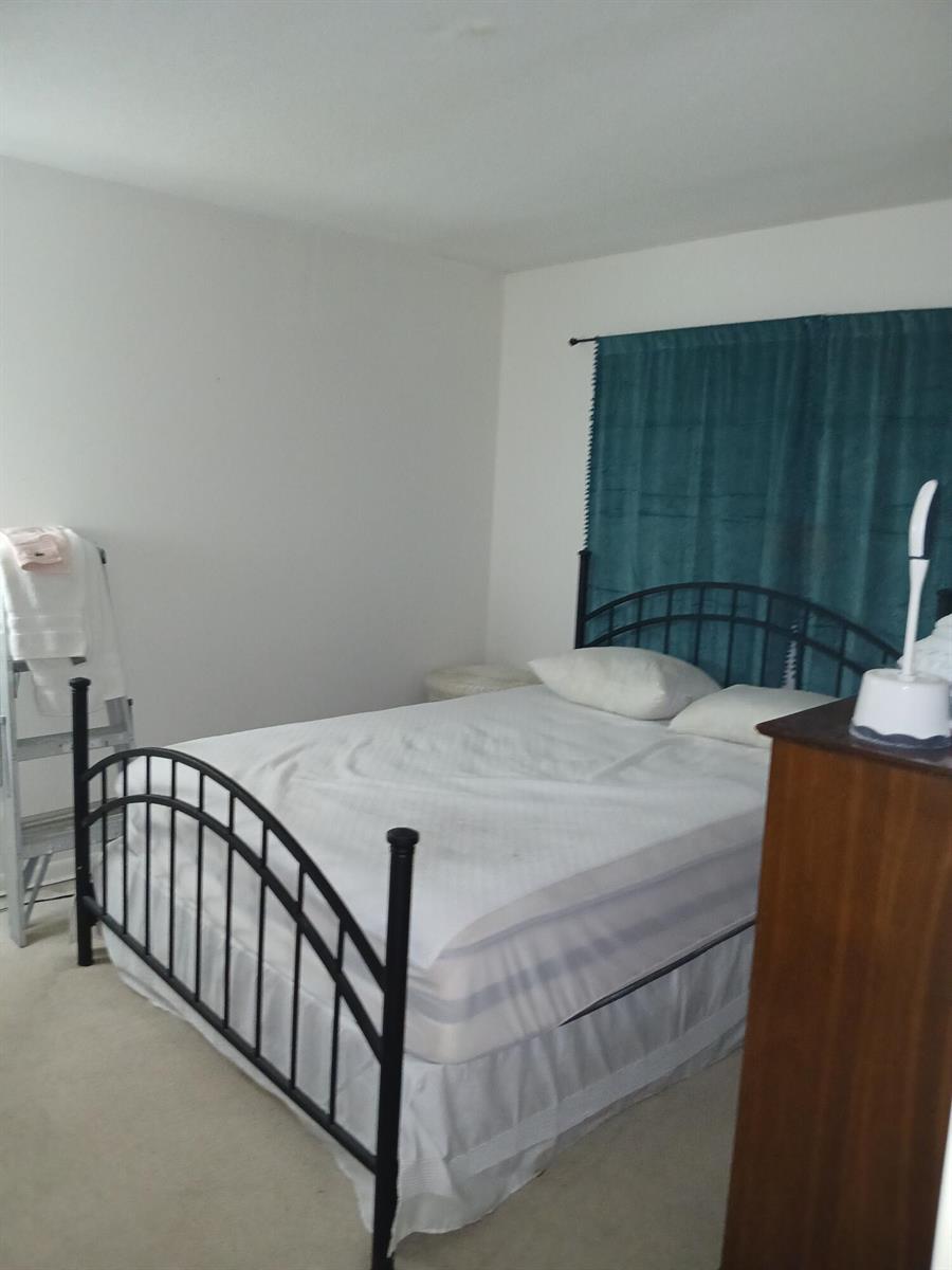 A bedroom features a black metal bed frame, white bedding, and teal curtains — 2601 NE 14th St Causeway # 233, Pompano Beach FL 33062, POMPANO BEACH, FL