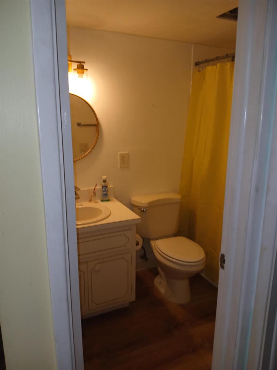 A small bathroom features a vanity with a round mirror, a toilet, and a yellow shower curtain — 2601 NE 14th St Causeway # 233, Pompano Beach FL 33062, POMPANO BEACH, FL