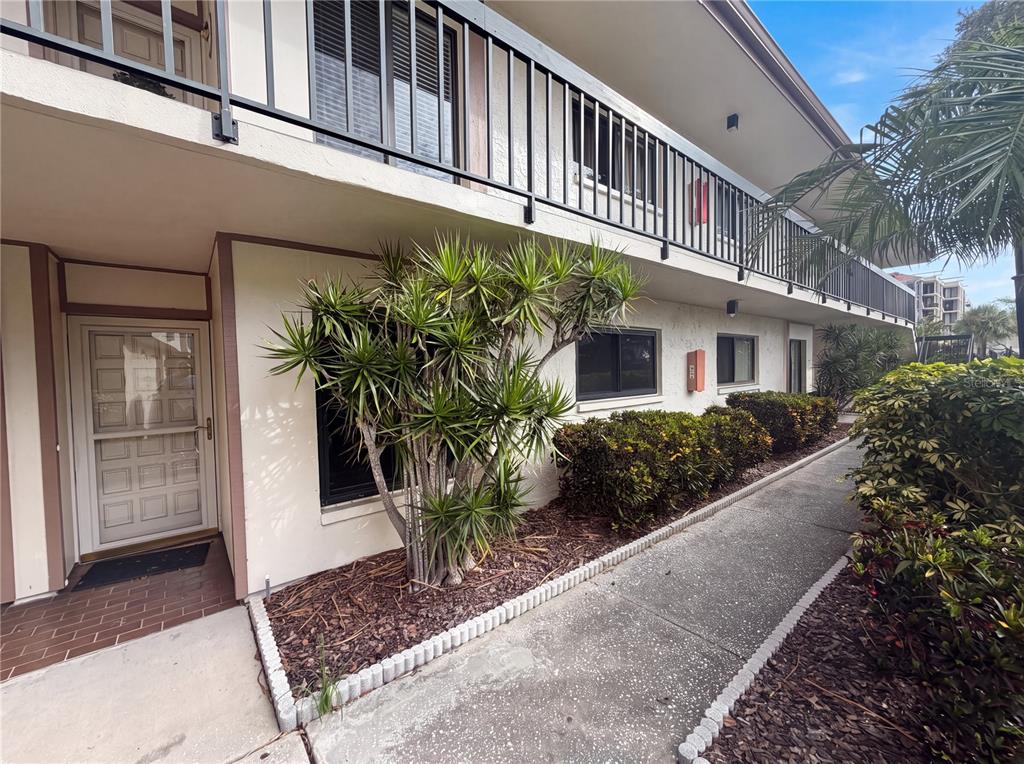 A two-story apartment building exterior features a concrete walkway, landscaping, and a second-floor balcony — 6219 PALMA DEL MAR BOULEVARD S UNIT 114, ST PETERSBURG, FL