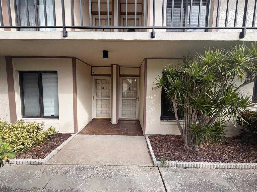 The exterior of a two-story building features two adjacent front doors and a large plant — 6219 PALMA DEL MAR BOULEVARD S UNIT 114, ST PETERSBURG, FL