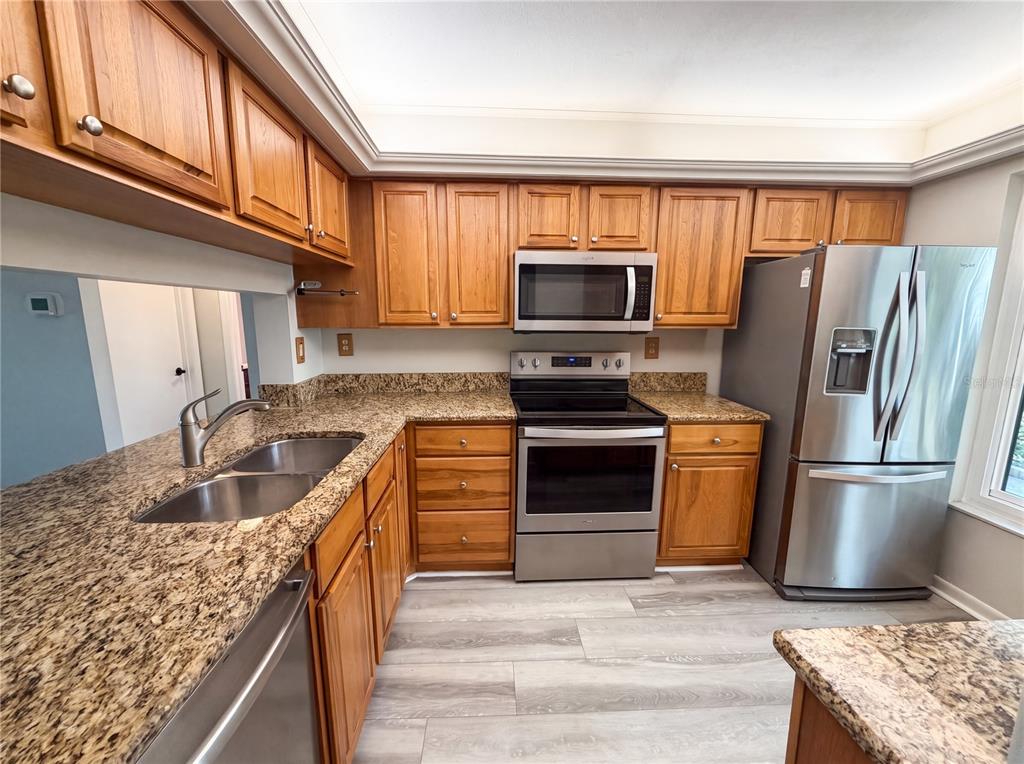 A kitchen features wood cabinets, granite countertops, stainless steel appliances, and light wood-look flooring — 6219 PALMA DEL MAR BOULEVARD S UNIT 114, ST PETERSBURG, FL