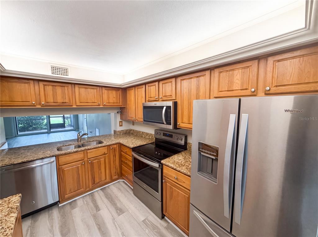 A kitchen features wood cabinets, granite countertops, stainless steel appliances, and light wood-look flooring — 6219 PALMA DEL MAR BOULEVARD S UNIT 114, ST PETERSBURG, FL