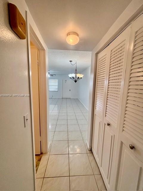 A hallway with white tile floors leads to a room featuring a decorative chandelier — 202 Mansfield, Boca Raton FL 33434, BOCA RATON, FL
