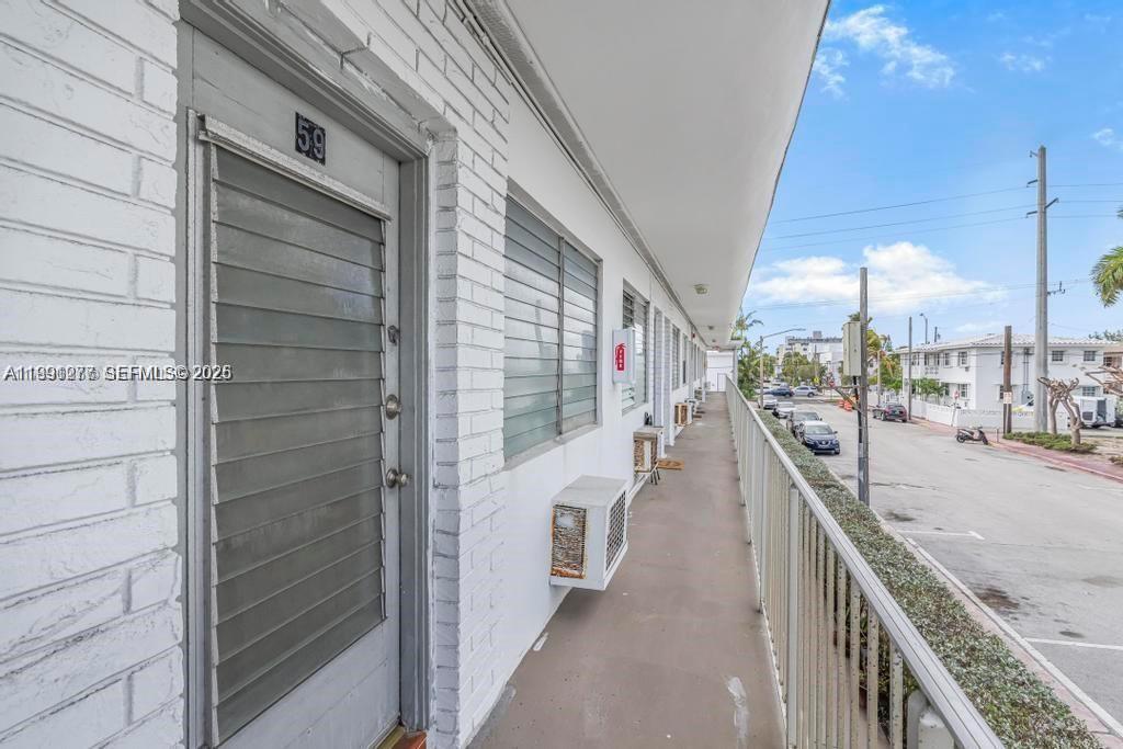 An exterior walkway with a brick wall, a numbered door, and windows overlooks a street — 200 76th St # 59, Miami Beach FL 33141, MIAMI BEACH, FL