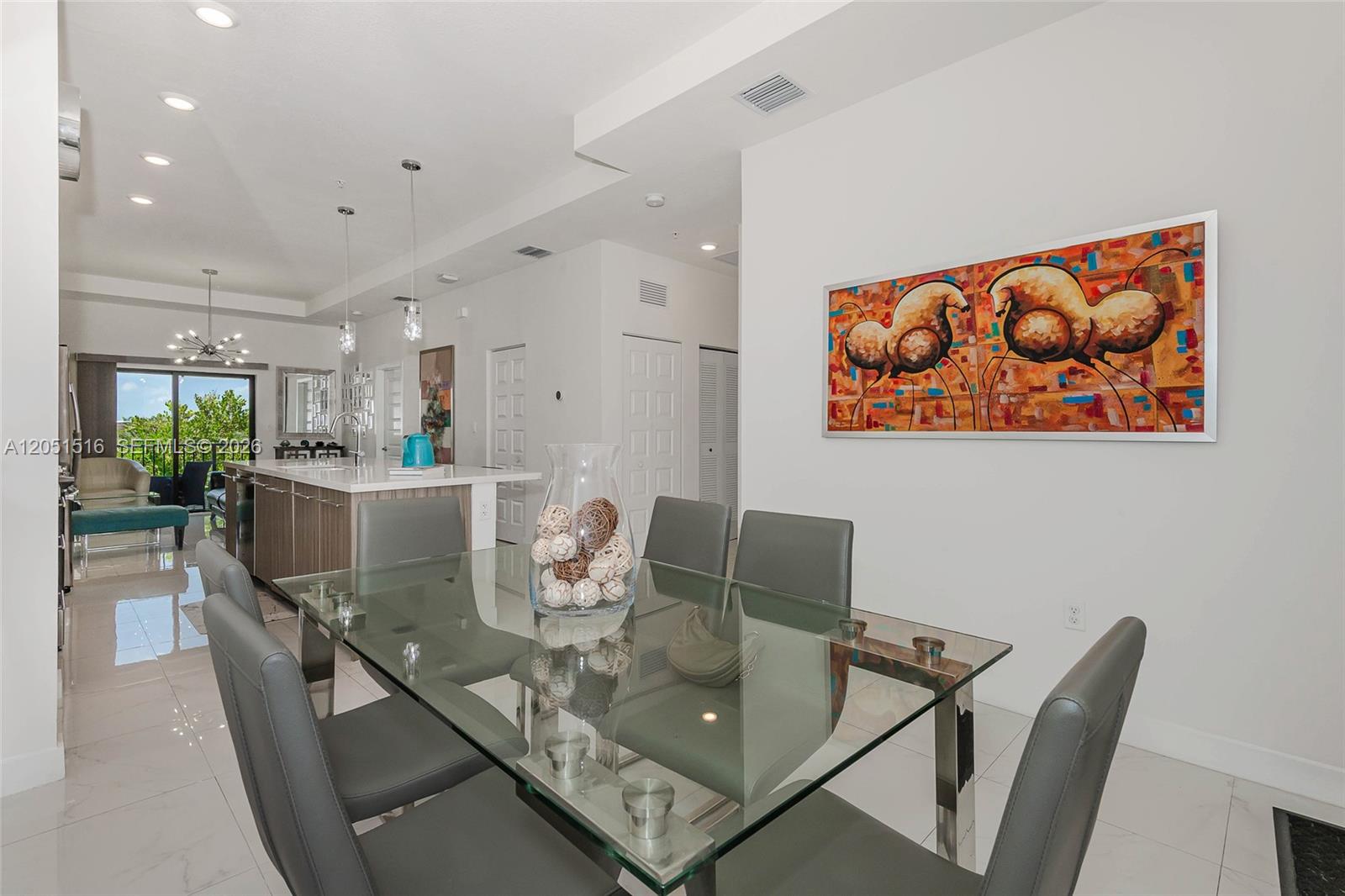 A dining area with a glass table and gray chairs sits before an open kitchen — 7815 NW 104th Ave # 34, Doral FL 33178, DORAL, FL