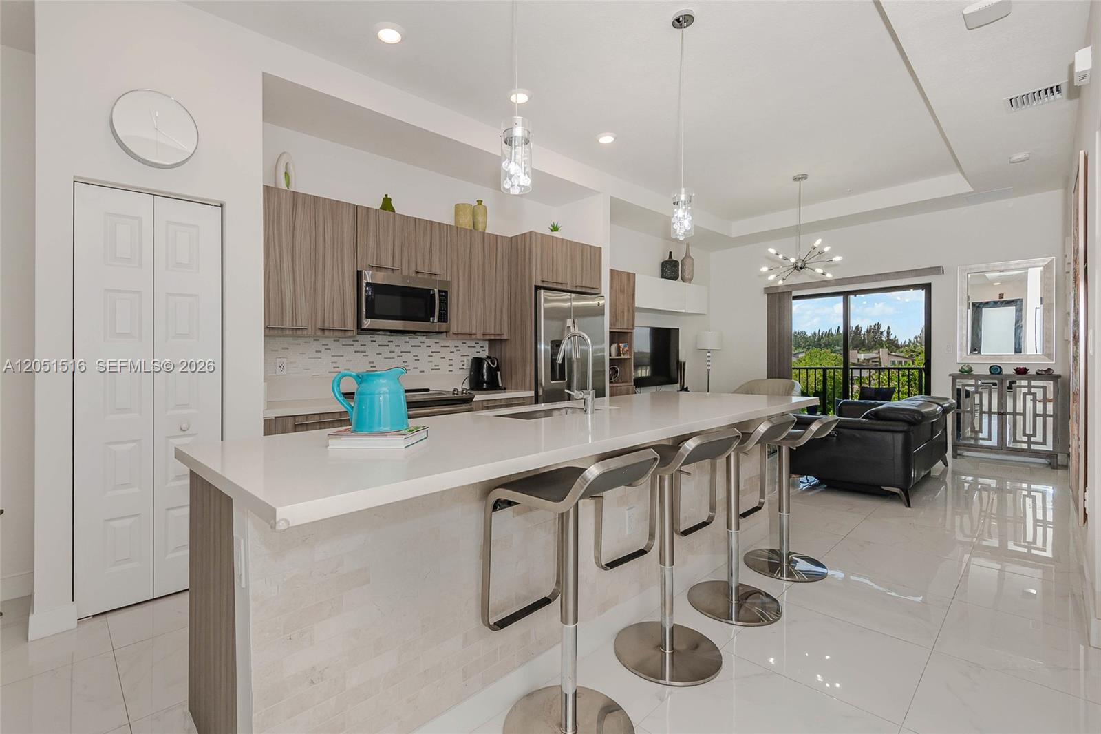 A modern kitchen features a white quartz island with bar stools and wood-toned cabinetry — 7815 NW 104th Ave # 34, Doral FL 33178, DORAL, FL