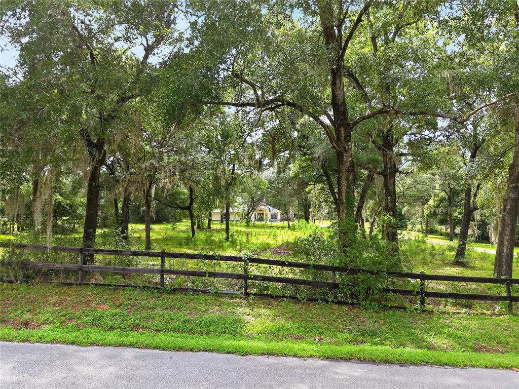 A wooden fence borders a grassy lot with mature trees and a house in the distance — 7300 SW 204TH AVENUE, DUNNELLON, FL