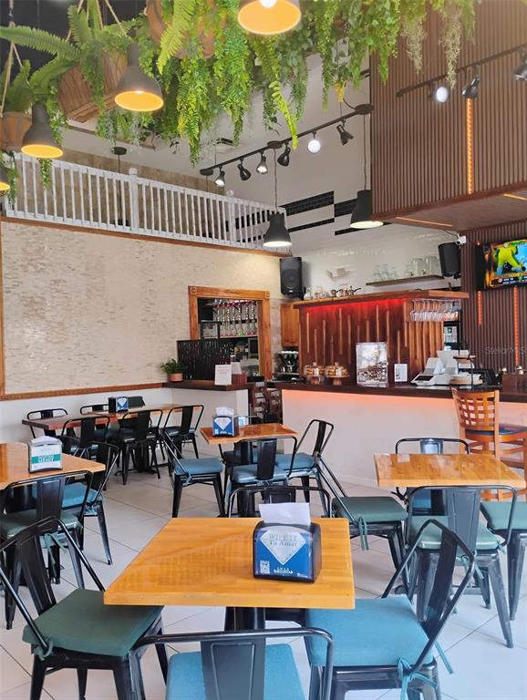 A restaurant interior features wooden tables, black metal chairs, hanging greenery, and a service bar — 8001 S ORANGE BLOSSOM TRAIL, ORLANDO, FL
