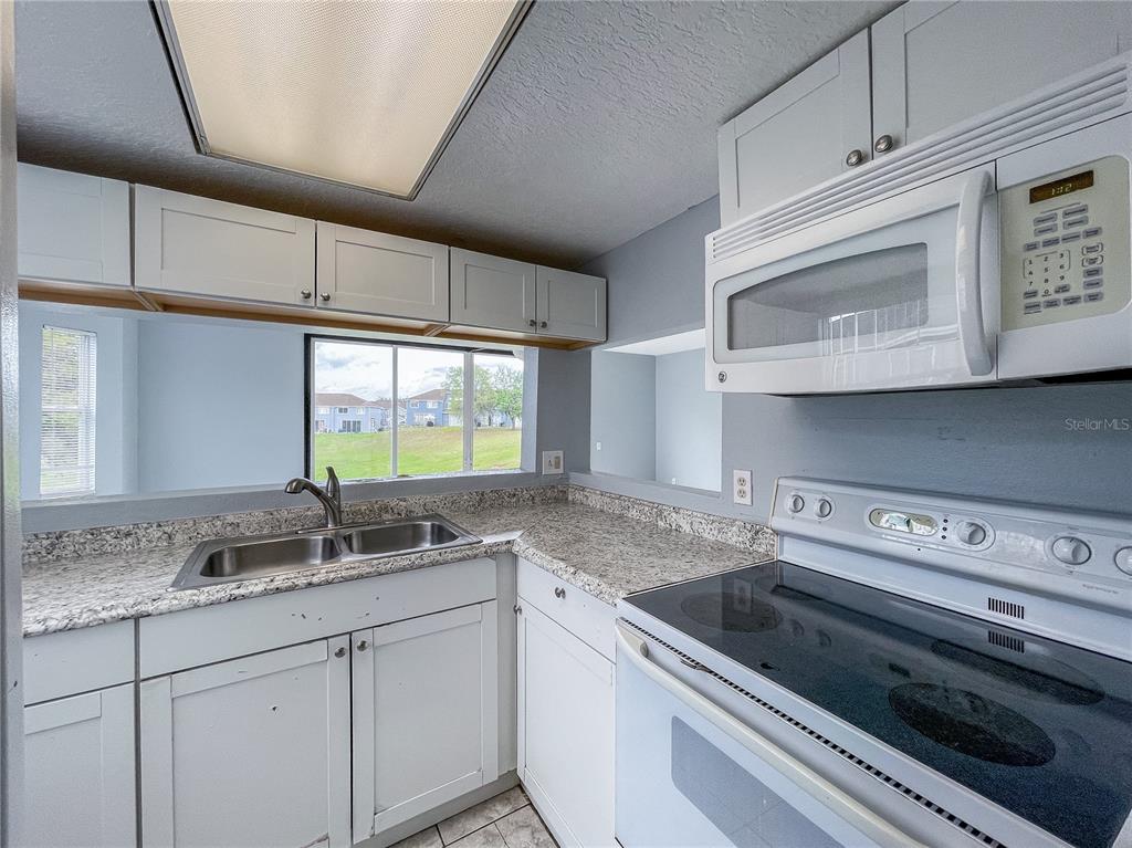 A kitchen features white cabinets, granite-look countertops, a double sink, and a microwave over the stove — 402 ORCHID DRIVE Main Unit, DAVENPORT, FL