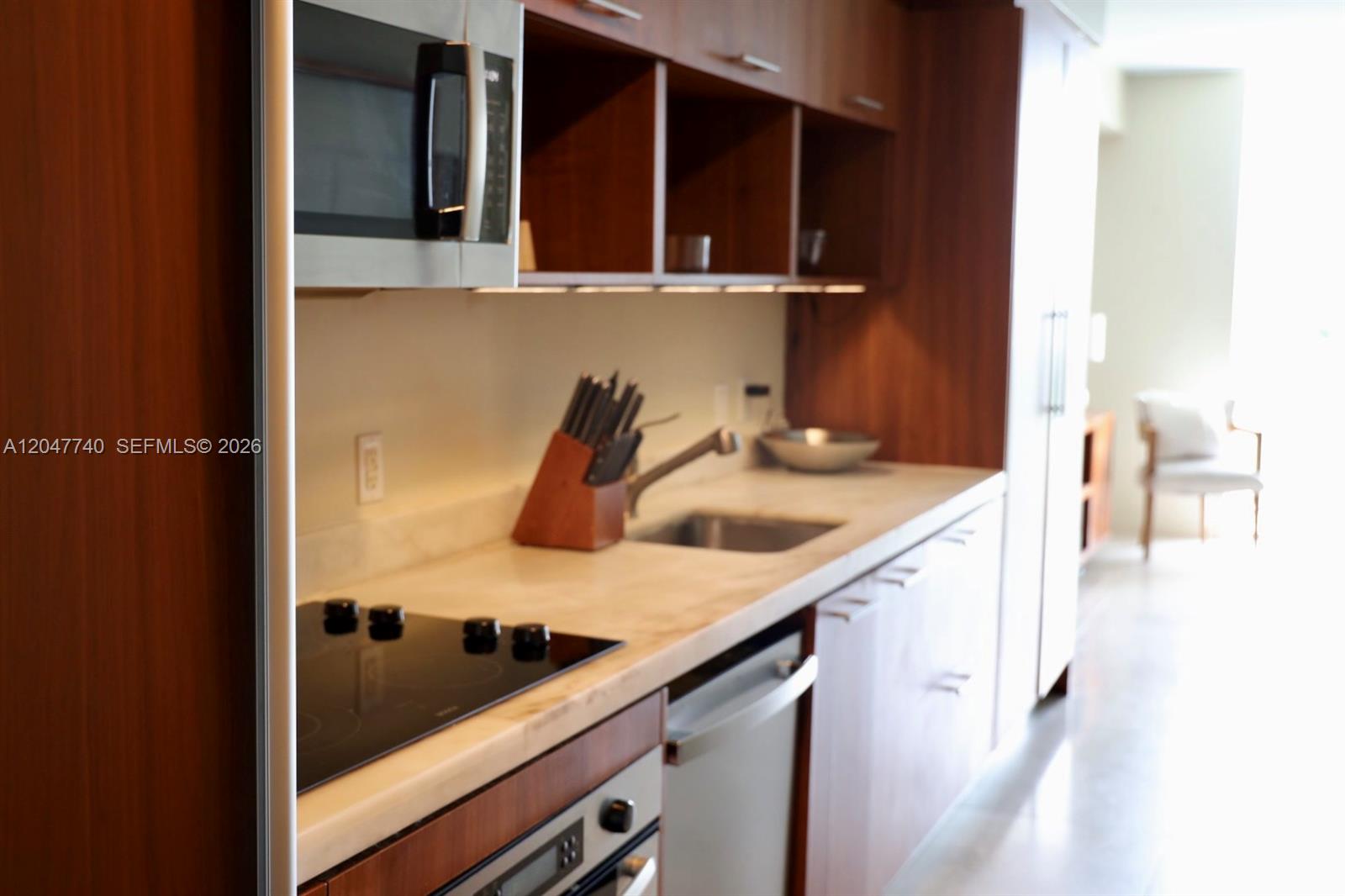 A modern kitchen features wood cabinets, a stainless steel microwave, and a black cooktop — 50 Biscayne Blvd # 606, Miami FL 33132, MIAMI, FL