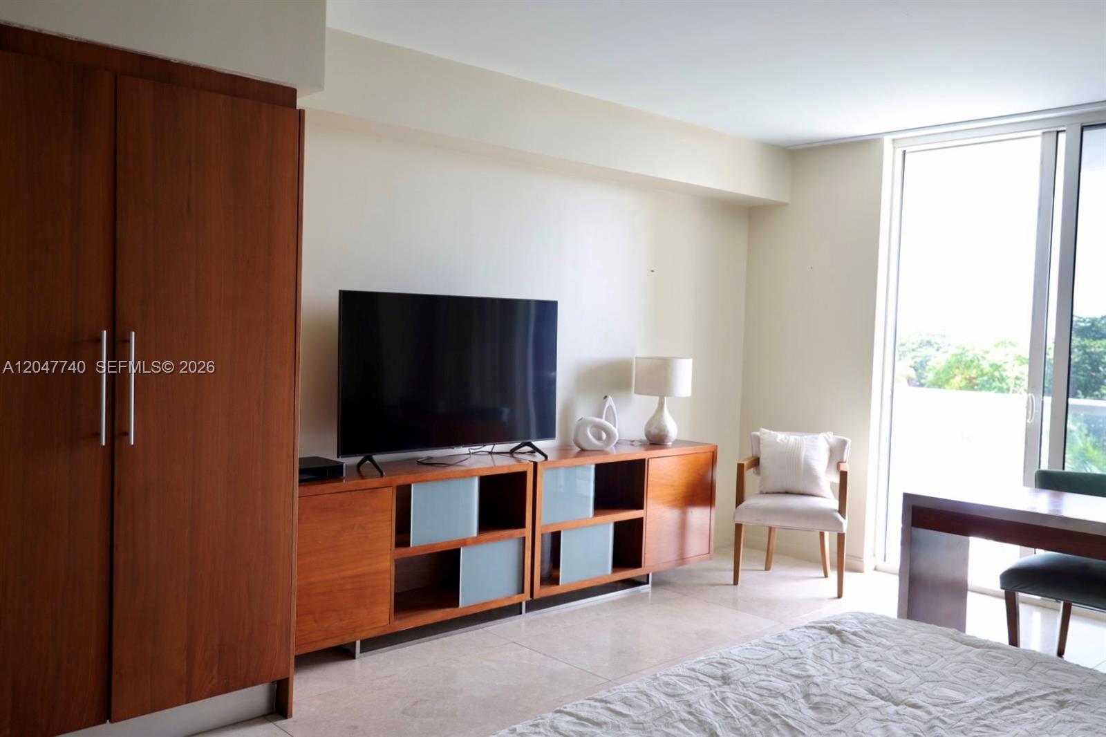 A bedroom features a wooden wardrobe, a media console with a television, and a chair — 50 Biscayne Blvd # 606, Miami FL 33132, MIAMI, FL