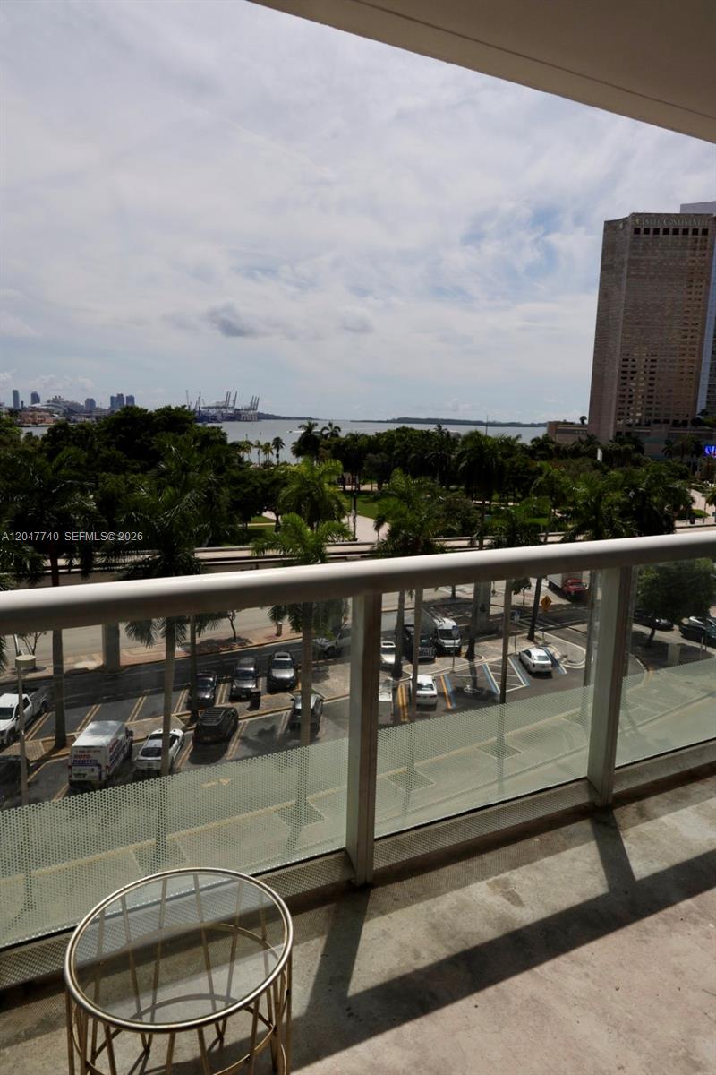 A balcony view overlooks a parking lot, palm trees, a bay, and a tall building — 50 Biscayne Blvd # 606, Miami FL 33132, MIAMI, FL