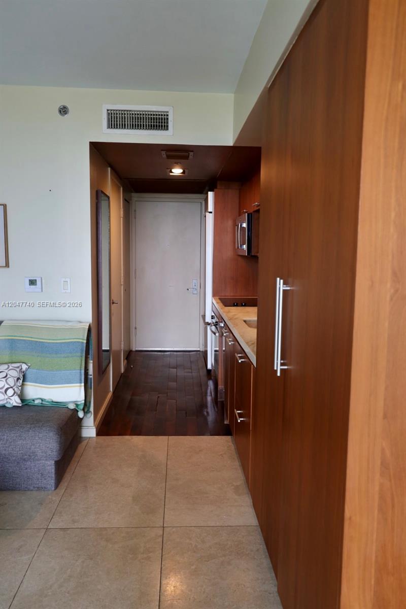A kitchen with wood cabinets and tile flooring leads to an entryway door — 50 Biscayne Blvd # 606, Miami FL 33132, MIAMI, FL