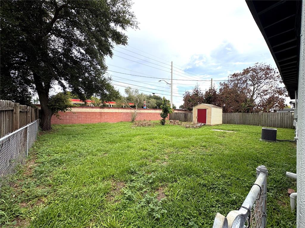 A grassy backyard features a storage shed, a large tree, and a red brick wall — 821 S SOLANDRA DRIVE, ORLANDO, FL