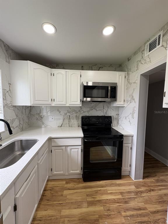 A kitchen features white cabinets, a black stove, a microwave, and marble-patterned wall tiles — 821 S SOLANDRA DRIVE, ORLANDO, FL