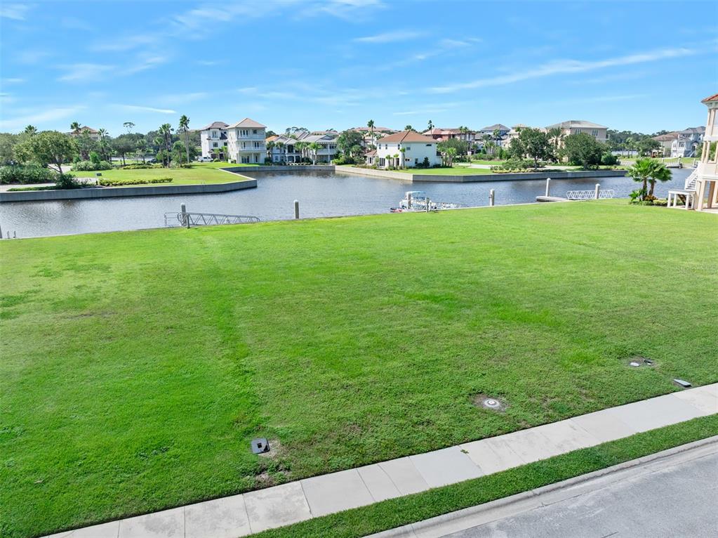 A vacant waterfront lot features a grassy lawn overlooking a canal and residential homes — 278 HARBOR VILLAGE POINT N, PALM COAST, FL