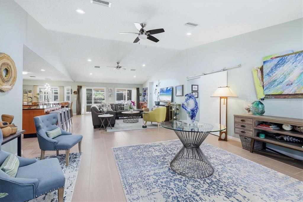 An open-concept living room features tile flooring, vaulted ceilings, and a glass-topped pedestal table — 1880 LOMA LINDA STREET, SARASOTA, FL