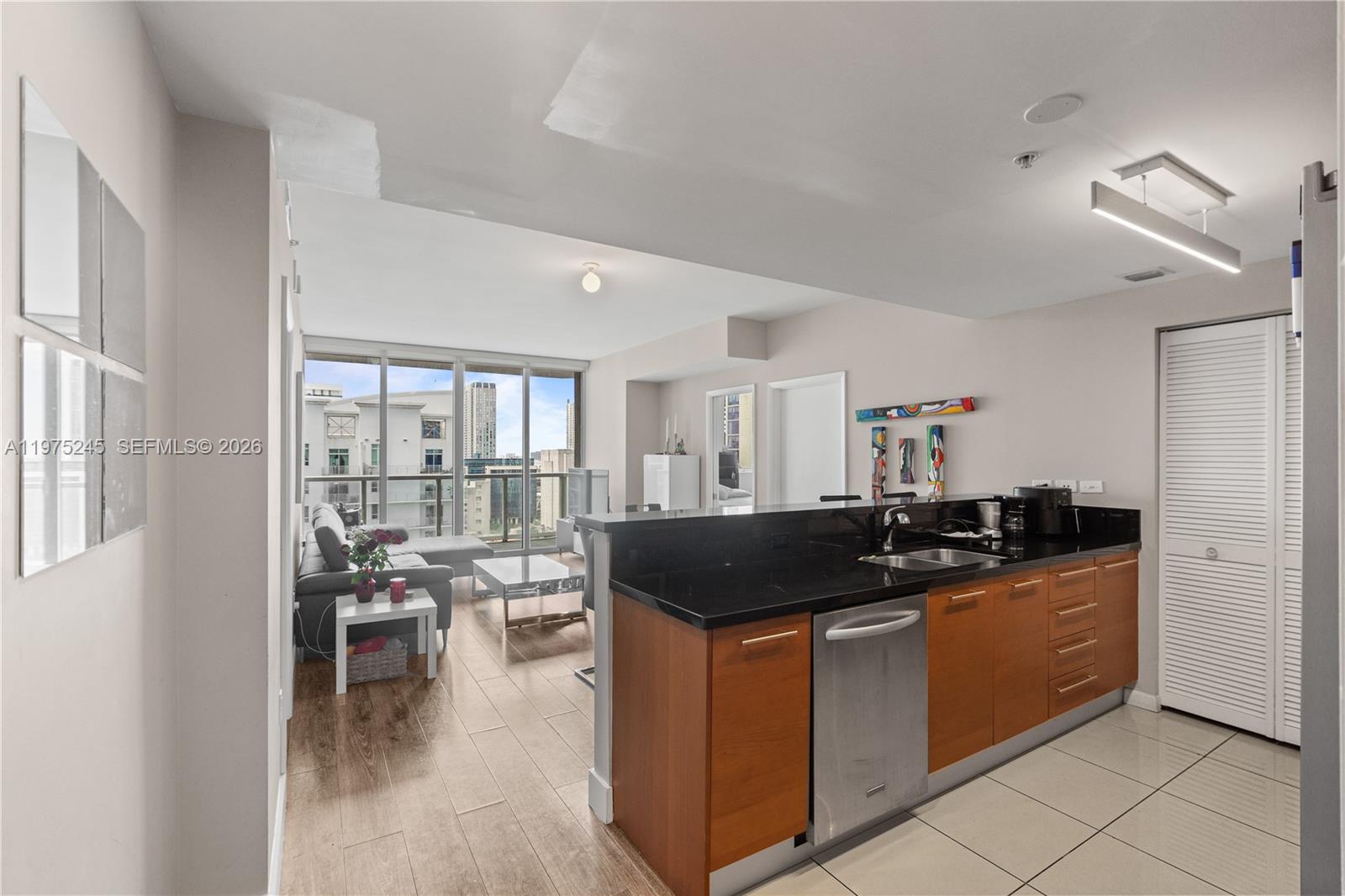A kitchen with dark countertops and wood cabinets opens into a living area with balcony — 244 Biscayne Blvd # 2410, Miami FL 33132, MIAMI, FL