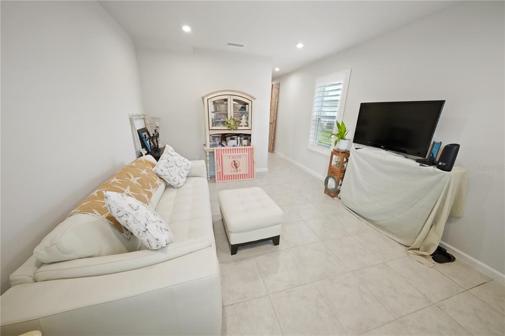A living room features a white sofa, a matching ottoman, and a television on a stand — 4175 HARBOUR PALM DRIVE, HOLIDAY, FL