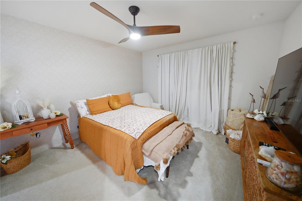 A bedroom features a bed with orange bedding, a ceiling fan, and a wooden console table — 4175 HARBOUR PALM DRIVE, HOLIDAY, FL