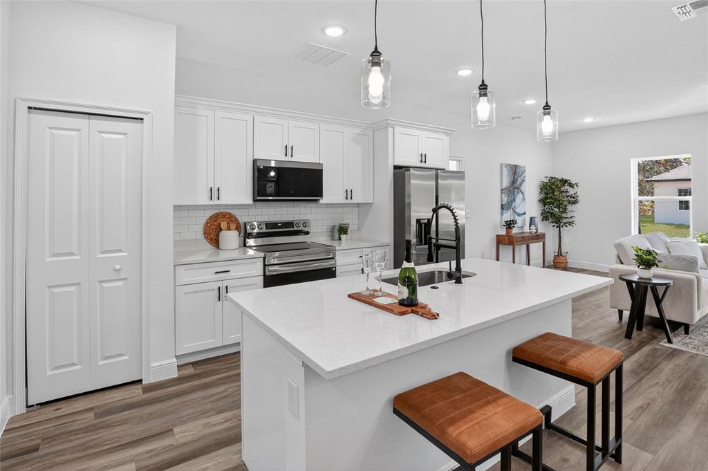A modern kitchen features white cabinets, a quartz island with bar stools, and stainless appliances — 8125 N MALTESE DRIVE, CITRUS SPRINGS, FL