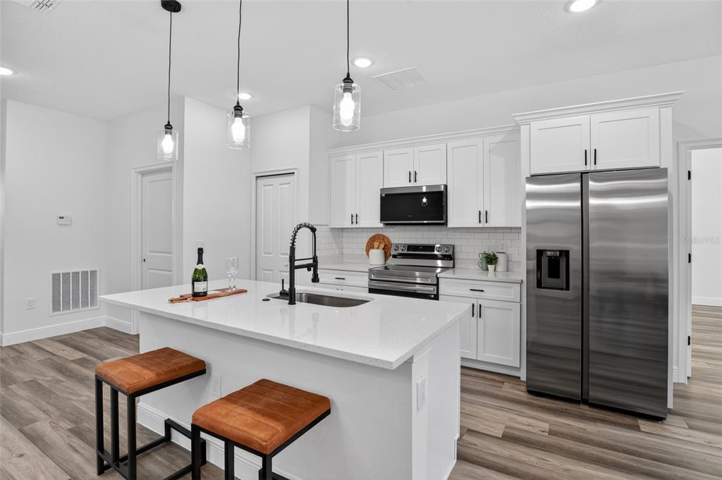 A modern kitchen features white cabinets, stainless steel appliances, a quartz island, and wood flooring — 8125 N MALTESE DRIVE, CITRUS SPRINGS, FL