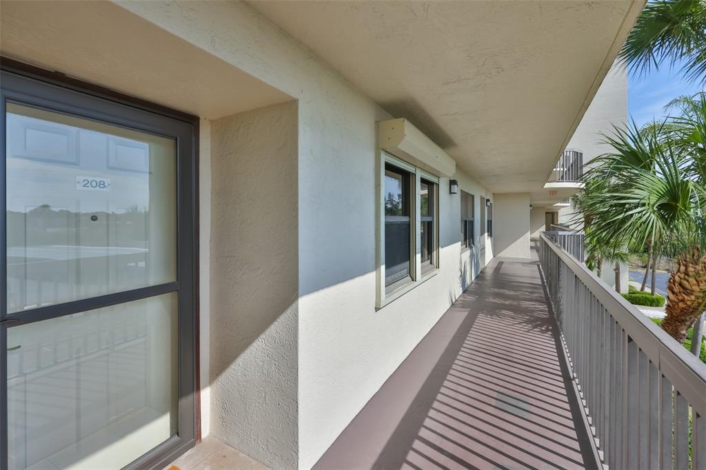 An exterior walkway with a metal railing leads past a door labeled 208 and windows — 5400 PARK STREET N UNIT 208, ST PETERSBURG, FL