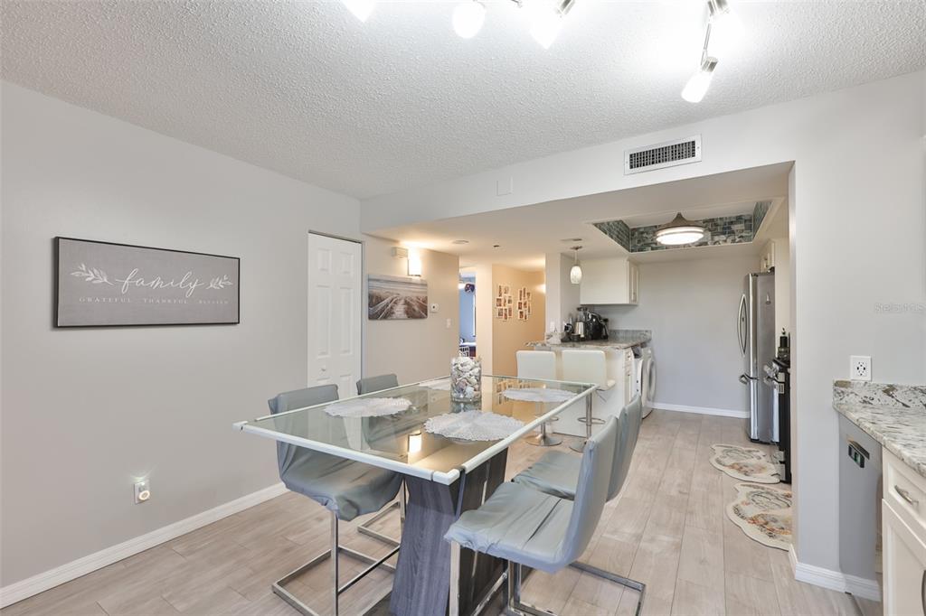 A dining area with a glass table and gray chairs opens into a kitchen — 5400 PARK STREET N UNIT 208, ST PETERSBURG, FL
