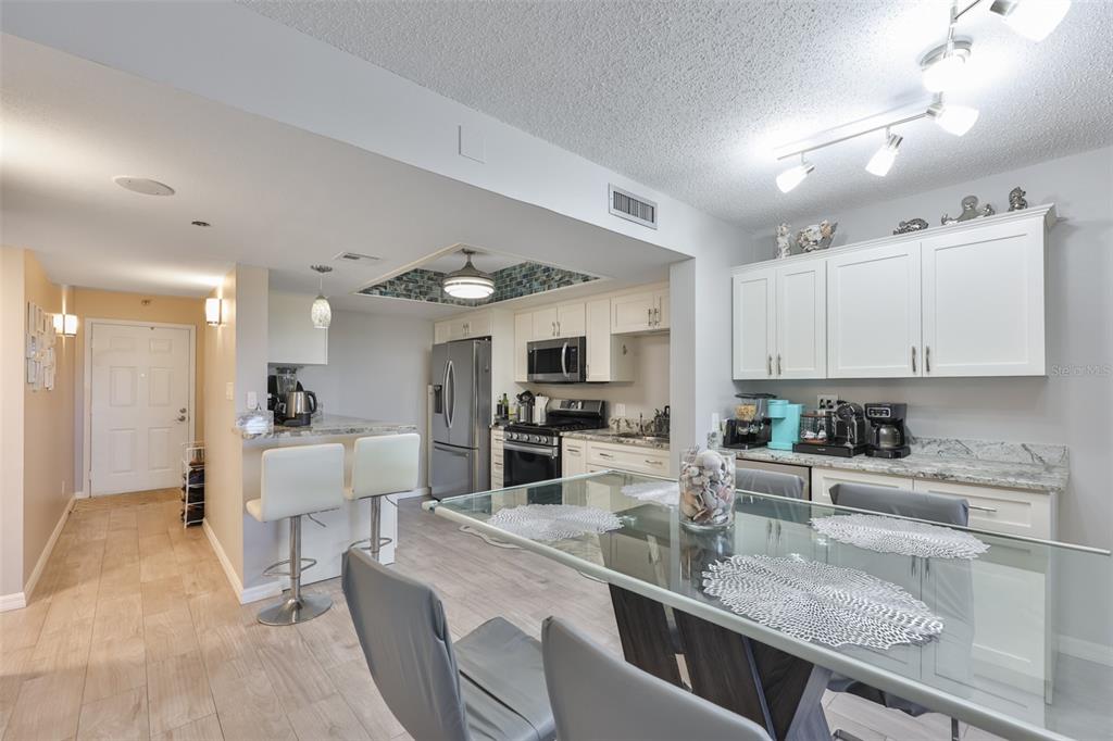 A kitchen and dining area featuring white cabinets, stainless steel appliances, and a glass table — 5400 PARK STREET N UNIT 208, ST PETERSBURG, FL