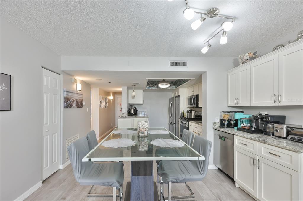 A dining area with a glass table and gray chairs sits adjacent to a kitchen — 5400 PARK STREET N UNIT 208, ST PETERSBURG, FL