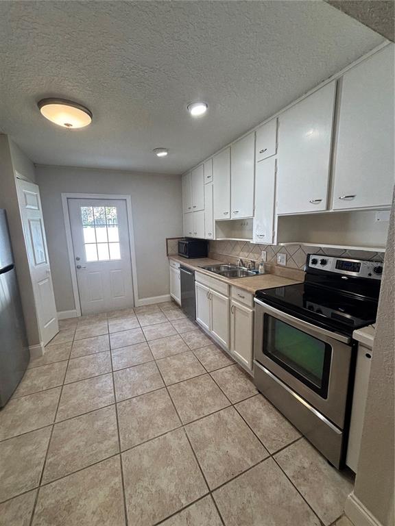 A kitchen features white cabinets, stainless steel appliances, and light-colored tile flooring — 1224 S GRAND HIGHWAY, CLERMONT, FL