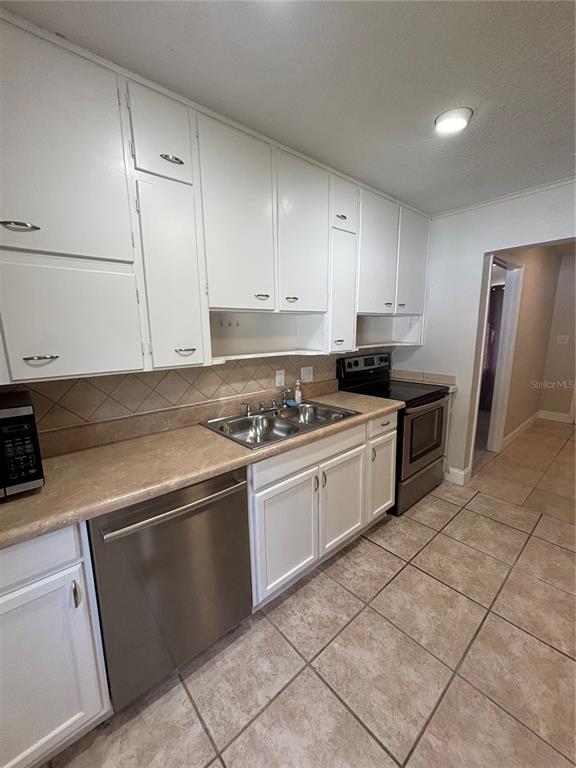 A kitchen features white cabinets, stainless steel appliances, a double sink, and tiled flooring — 1224 S GRAND HIGHWAY, CLERMONT, FL