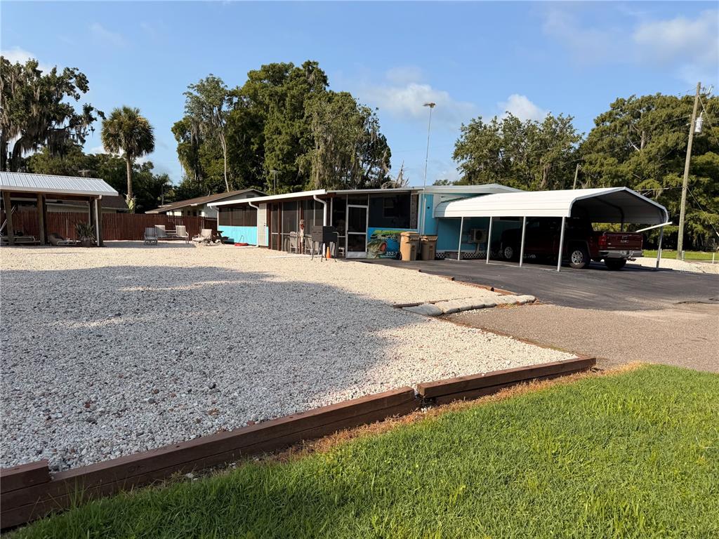 A single-story house with a gravel yard, a carport, and a screened-in porch — 56350 ACORN ROAD, ASTOR, FL