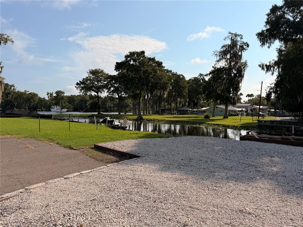 A gravel driveway leads to a grassy lawn bordering a canal with trees and houses — 56350 ACORN ROAD, ASTOR, FL