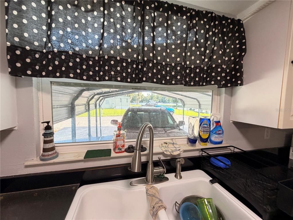 A kitchen sink area features a window with polka-dot curtains overlooking a carport — 56350 ACORN ROAD, ASTOR, FL