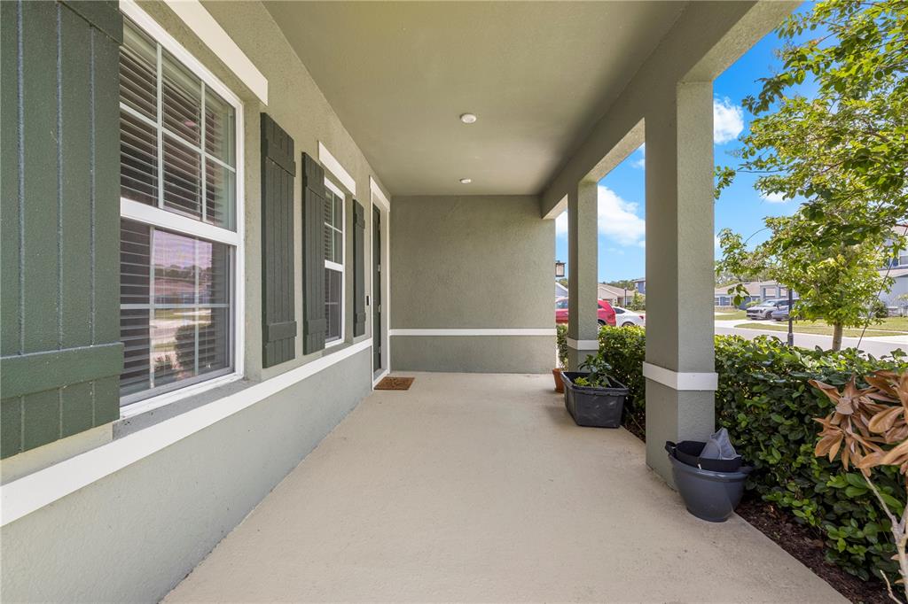 A covered front porch with a concrete floor, green stucco walls, and dark shutters — 7878 GREENWAY AVENUE, WESLEY CHAPEL, FL