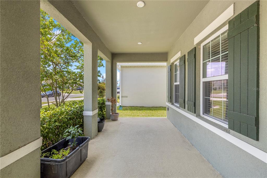 A covered front porch with green stucco walls, dark shutters, and potted plants — 7878 GREENWAY AVENUE, WESLEY CHAPEL, FL