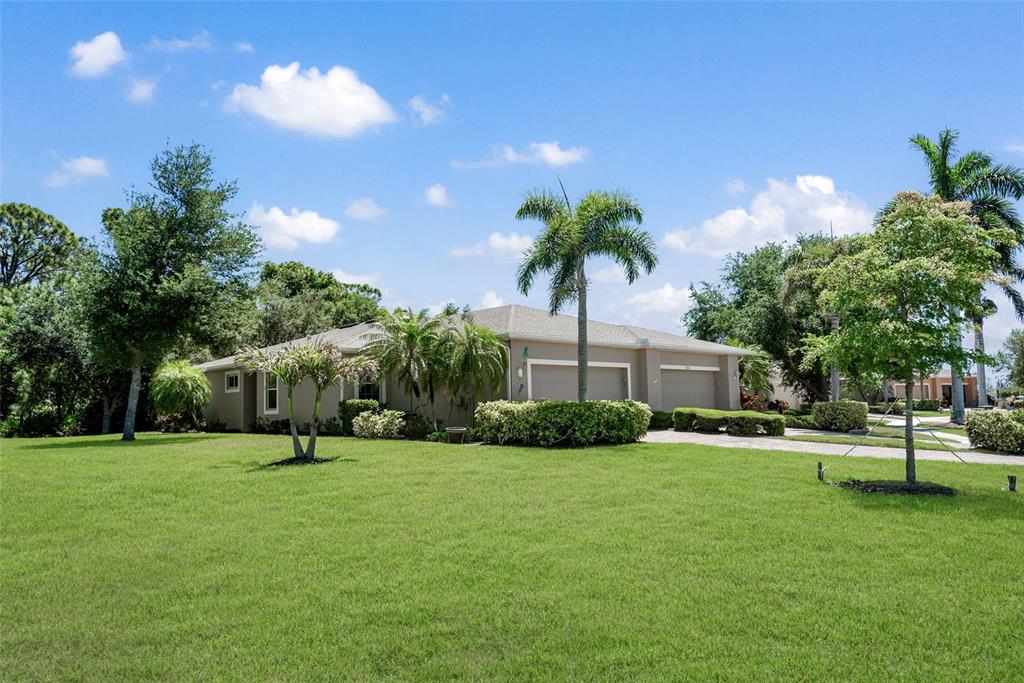 A tan single-story house with a two-car garage sits behind a large green lawn — 29696 ONTARIO COURT, ENGLEWOOD, FL