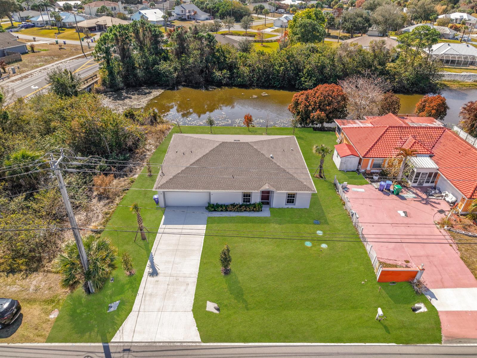 An aerial view shows a single-story house with a gray roof, driveway, and large lawn — 1390 Schumann Drive, Sebastian FL 32958, SEBASTIAN, FL