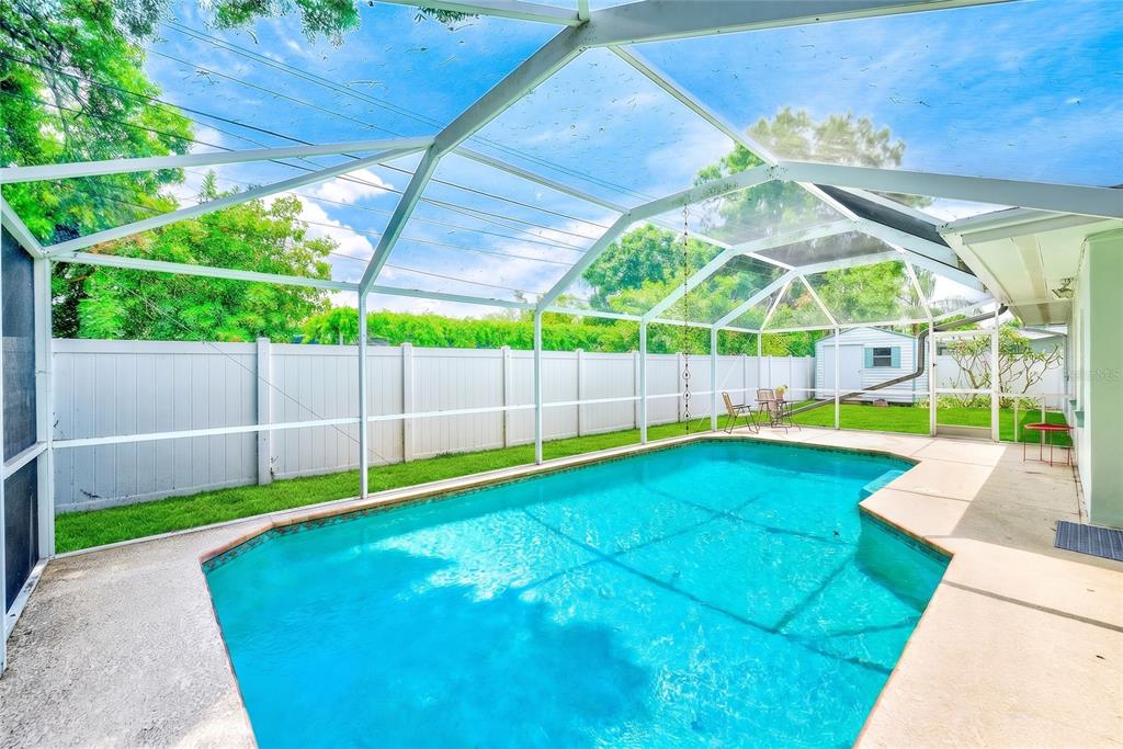 A swimming pool with a screened enclosure sits in a backyard with a white fence — 3255 57TH STREET N, ST PETERSBURG, FL