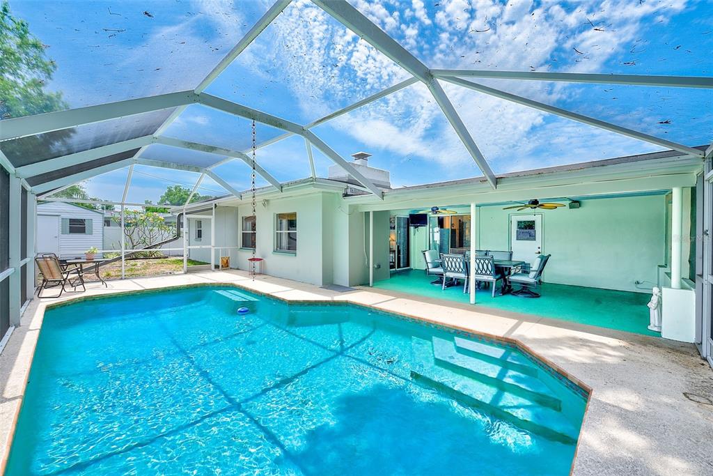 A swimming pool sits inside a screened-in patio area with a covered outdoor dining space — 3255 57TH STREET N, ST PETERSBURG, FL