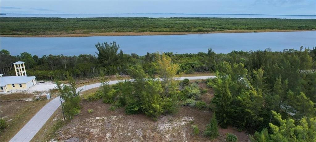 An aerial view shows a vacant, wooded lot near a body of water and a house — 16285 RENNIE ROAD, PORT CHARLOTTE, FL