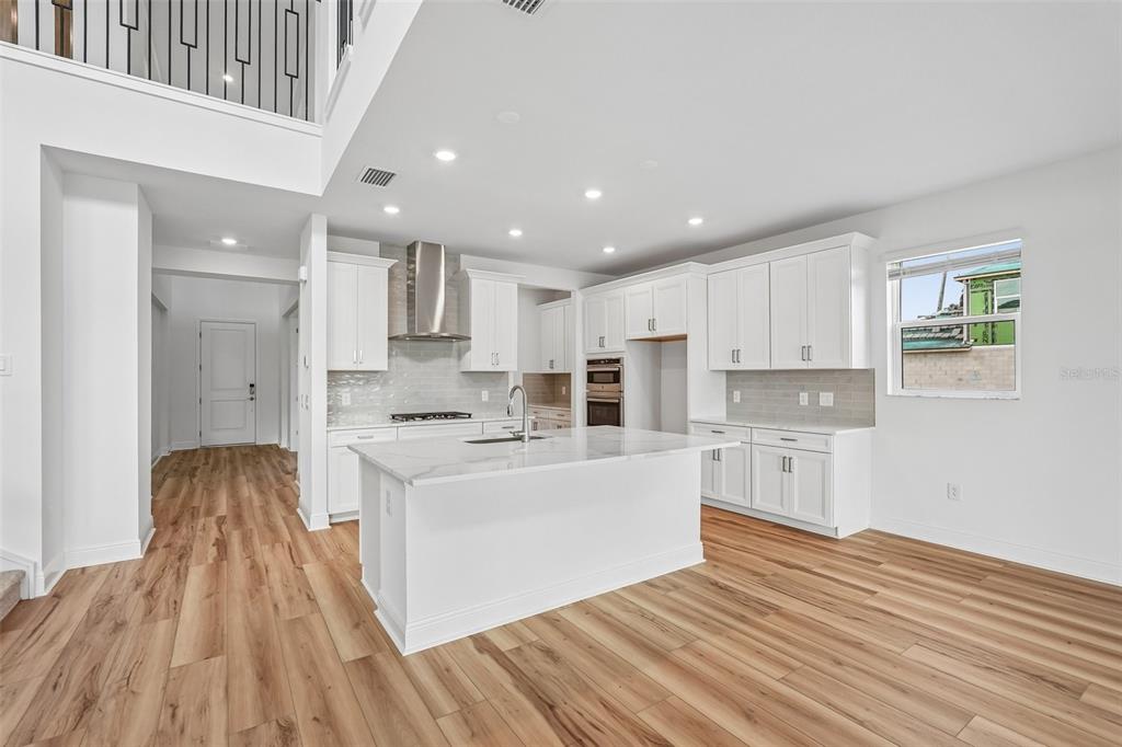 A bright kitchen features white cabinetry, a marble-topped island, and light wood-look flooring — 7660 SEAHAWK AVENUE, SARASOTA, FL
