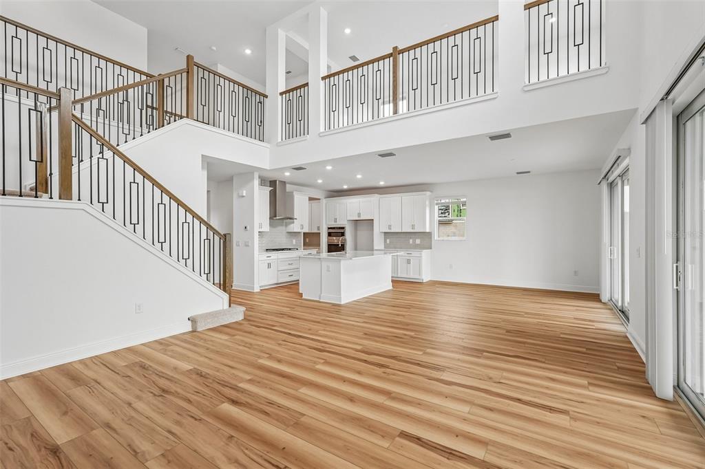 An open-concept living area features light wood floors, a white kitchen, and a grand staircase — 7660 SEAHAWK AVENUE, SARASOTA, FL