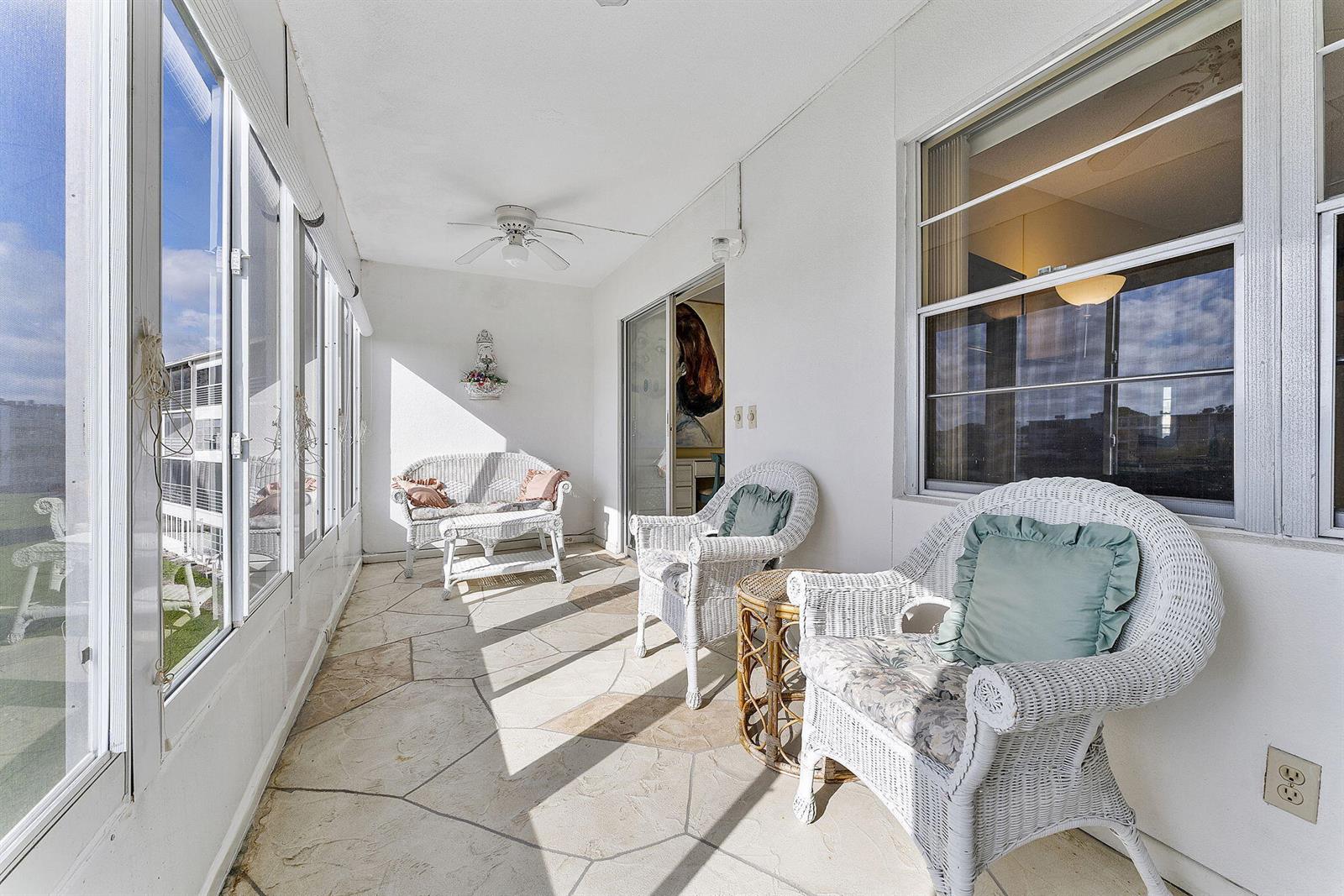 A sunroom features white wicker furniture, a stone floor, and large windows overlooking the exterior — 3027 Guildford B, Boca Raton FL 33434, BOCA RATON, FL
