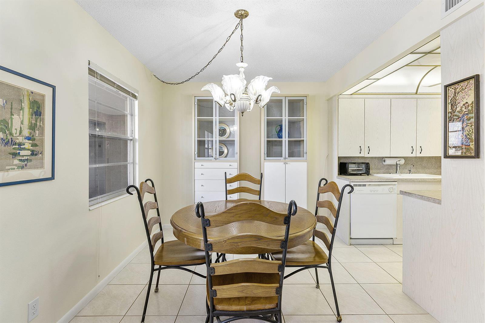 A dining area features a round wooden table, four chairs, and built-in glass-front cabinets — 3027 Guildford B, Boca Raton FL 33434, BOCA RATON, FL
