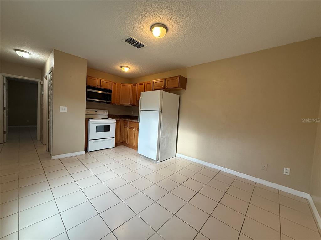 A kitchen with light-colored tile flooring, wooden cabinets, white appliances, and beige walls — 601 HARDY STREET UNIT 8, BUNNELL, FL